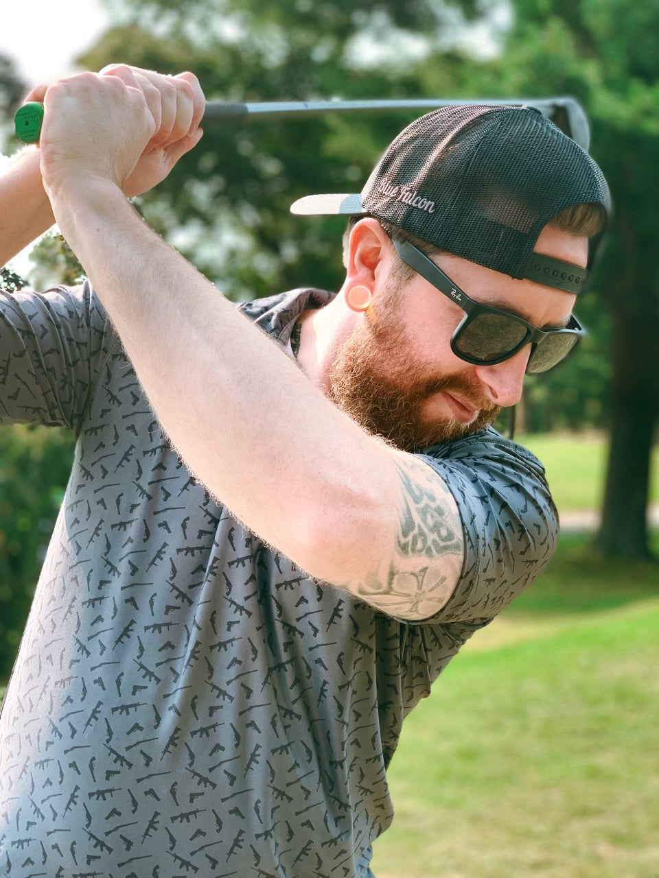 A dark gray performance polo featuring a variety of rifle and pistol icon designs in various sizes and placements.