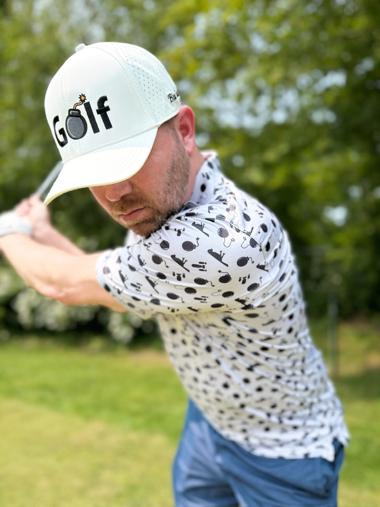 A man swinging a golf club wearing the Blue Falcon "Birdie Bomber" hat and the "Bombs Away" polo shirt.