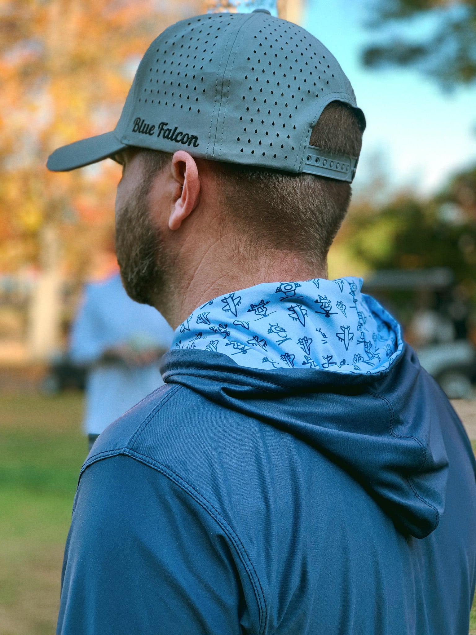 A golfer in a hat and performance hoodie with a graphic design inside the hood, facing away from the camera on a golf course.