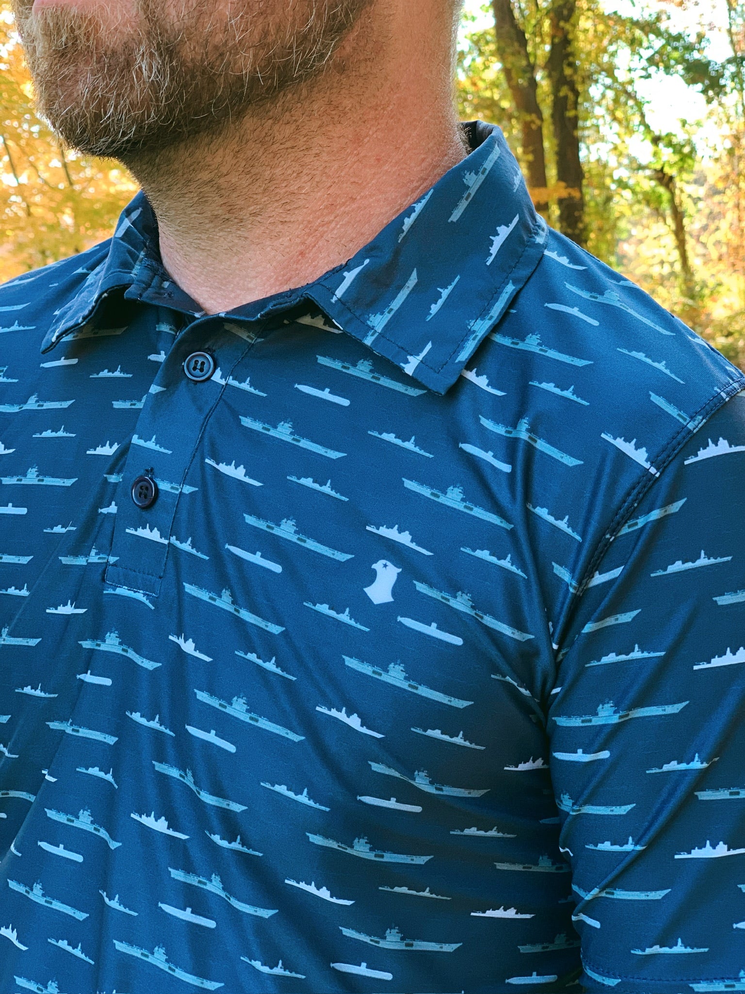 Close up of blue performance polo with ship and submarine icons and blue falcon logo on left chest.