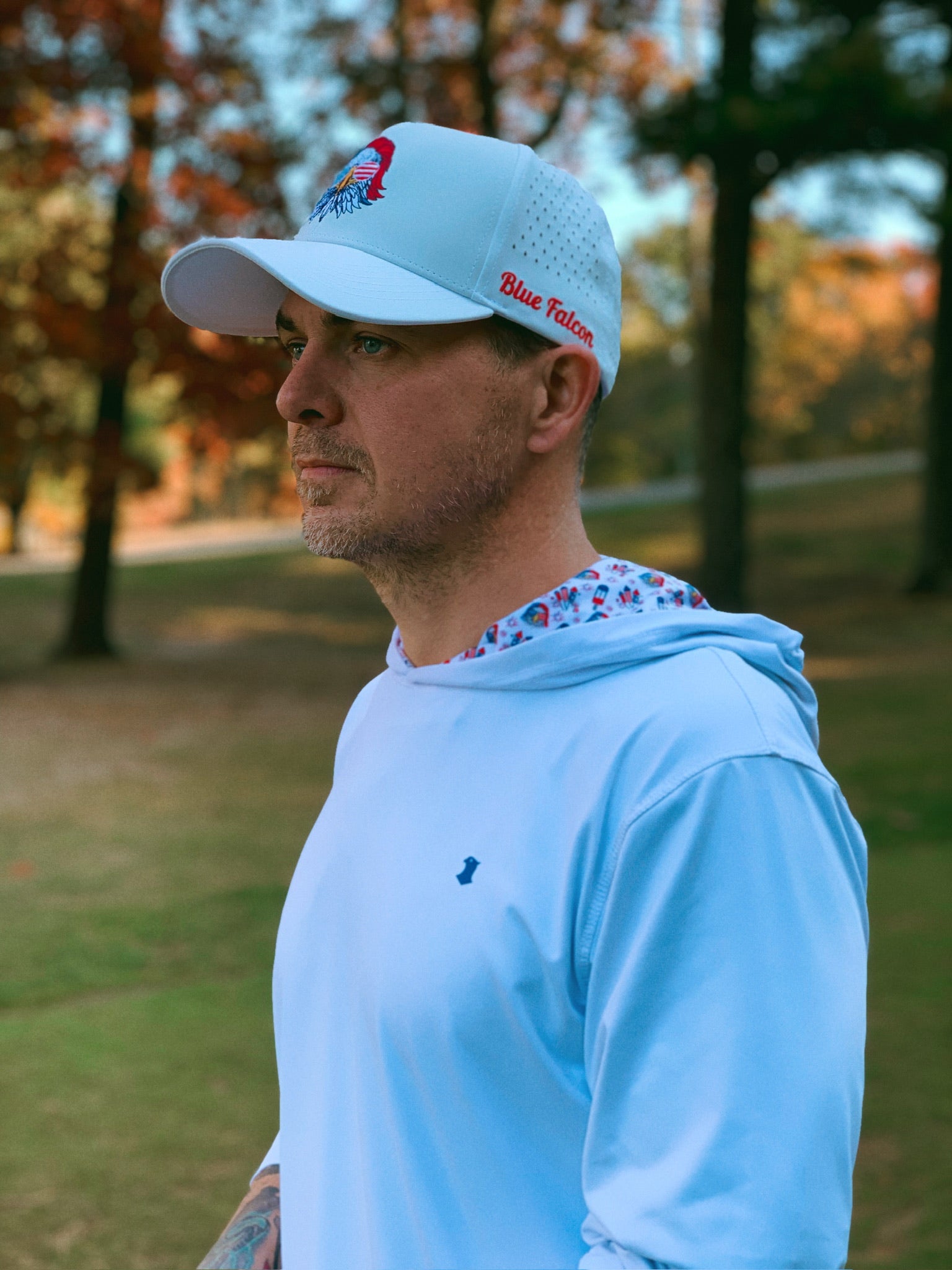 A golfer in a hat and performance hoodie, with a pop of graphic design on the inside of the hood, standing looking off into the distance.