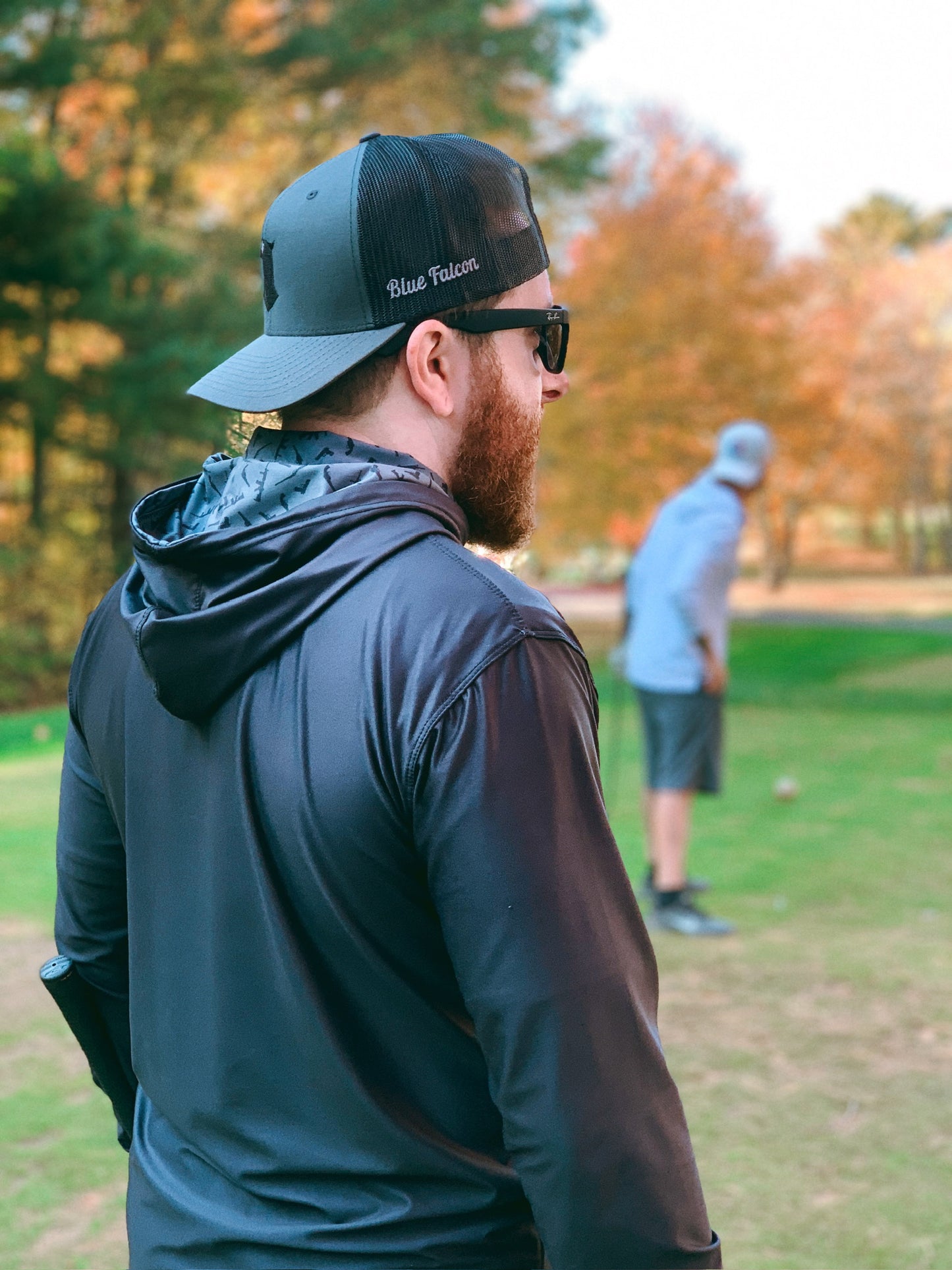 A golfer in a hat and performance hoodie, with a pop of graphic design on the inside of the hood, standing on the green.