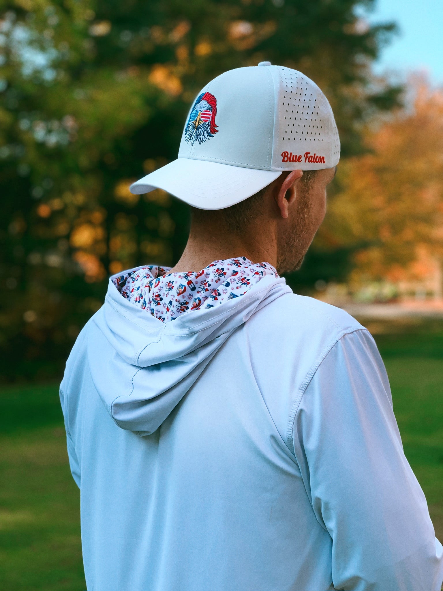 A golfer wearing a white performance hoodie featuring patriotic symbols inside the hood and a white performance hat with a patriotic eagle and "Blue Falcon" written on the side.